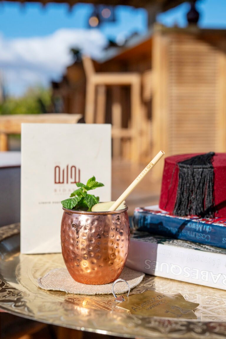 A signature cocktail in a copper mug with fresh mint, served at Bidaya Rooftop Bar in Marrakech, featuring a traditional red fez and Moroccan art books
