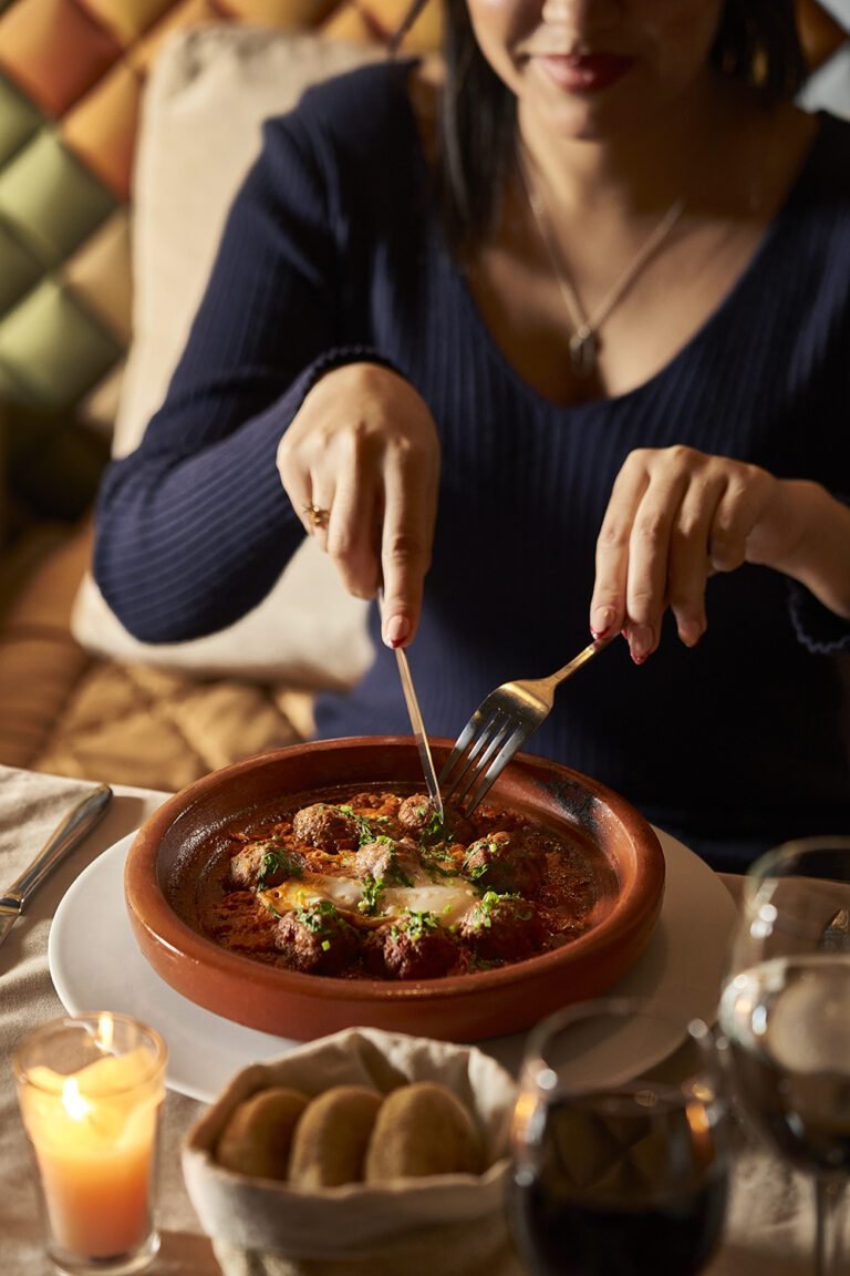 A guest enjoying a traditional Kefta tajine with eggs at the Pixel Restaurant, Almaha Marrakech, in a cozy candlelit atmosphere