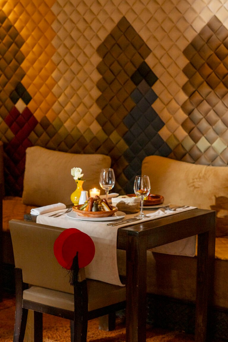 Traditional Moroccan tajine and fine dining setting for two at the Pixel Restaurant, Almaha Marrakech, with a geometric silk-tiled wall in the background